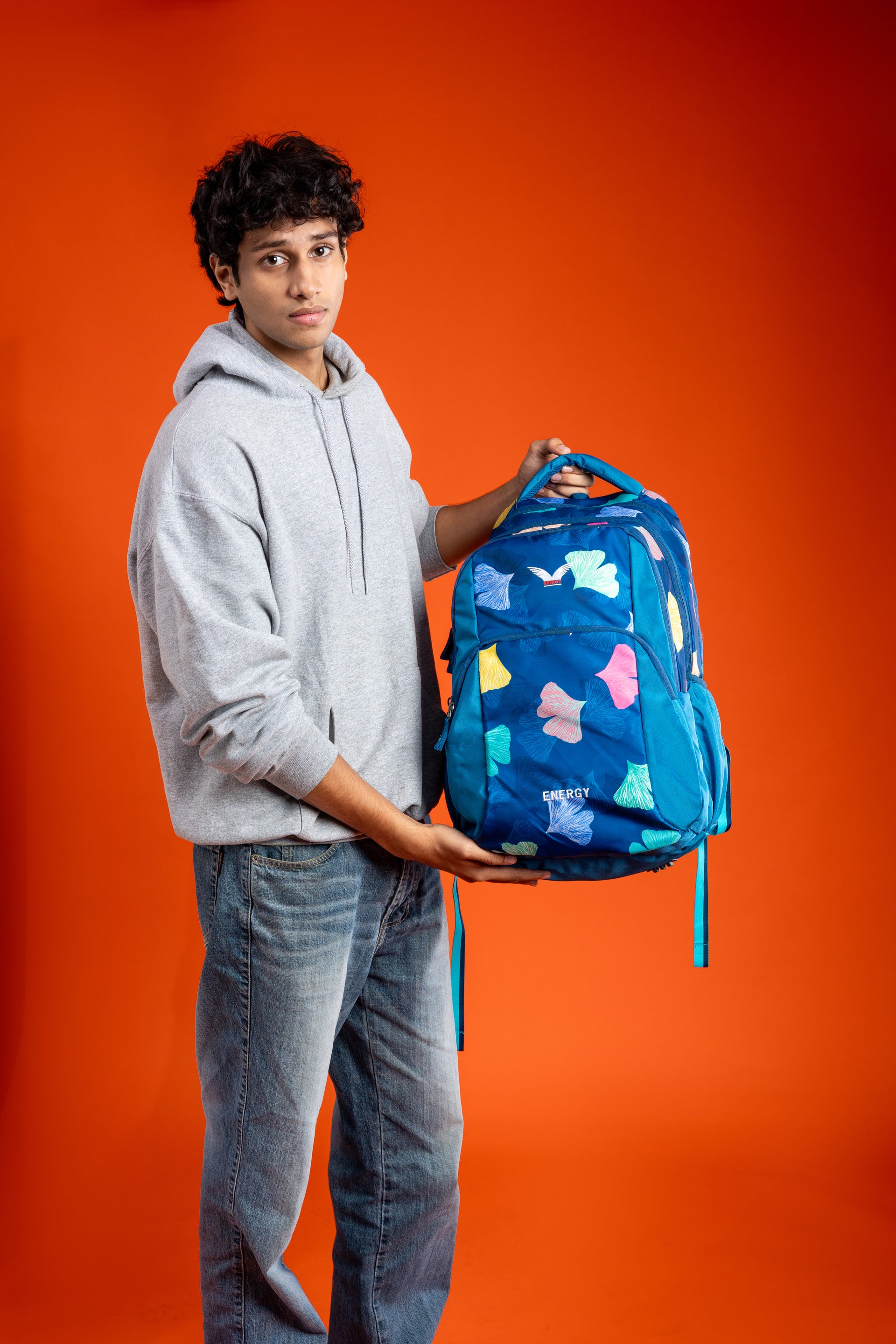Person holding a blue backpack against an orange background